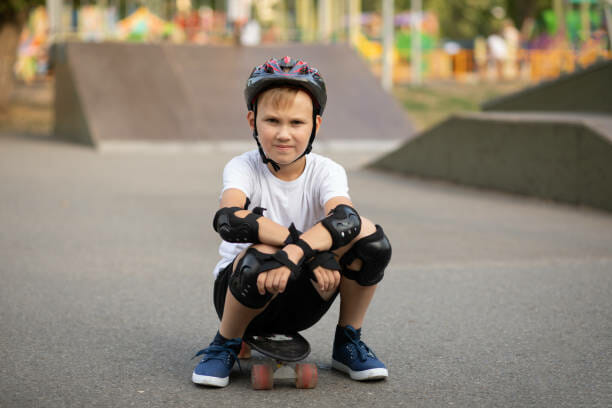 Cute kid boy child in a helmet sitting in a special area in skate park and holding skateboard